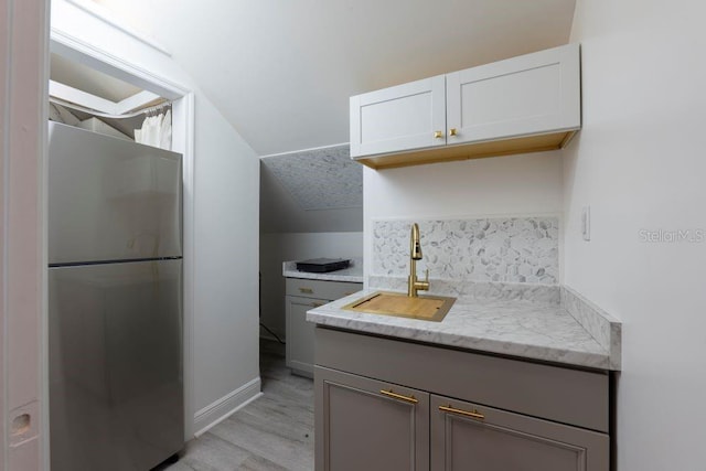 kitchen featuring white cabinets, lofted ceiling, stainless steel fridge, sink, and light wood-type flooring