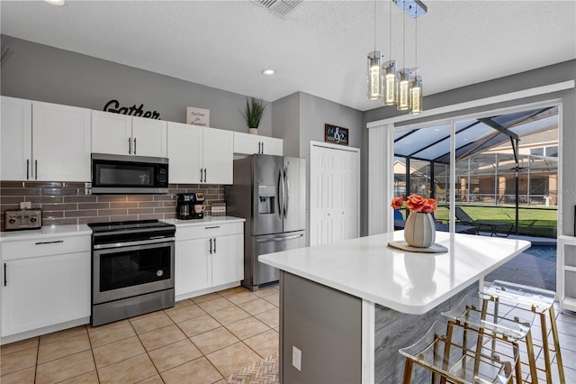 kitchen with white cabinets, a breakfast bar area, stainless steel appliances, a center island, and decorative light fixtures