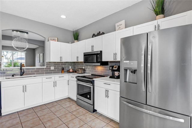 kitchen with white cabinets, sink, backsplash, stainless steel appliances, and an inviting chandelier