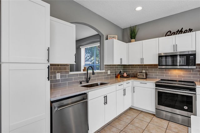 kitchen with appliances with stainless steel finishes, white cabinetry, light tile patterned floors, a textured ceiling, and sink