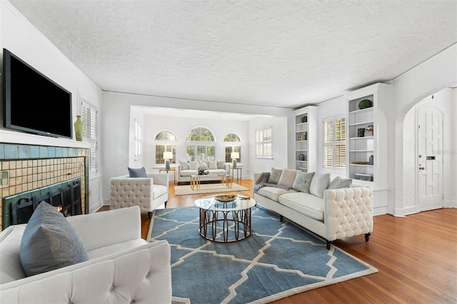 living room featuring built in shelves, wood-type flooring, and a textured ceiling