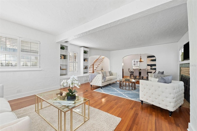 living room with built in shelves, wood-type flooring, a textured ceiling, and a brick fireplace