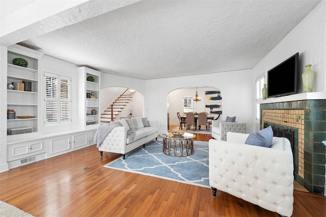 living room with built in shelves, wood-type flooring, a textured ceiling, and a brick fireplace