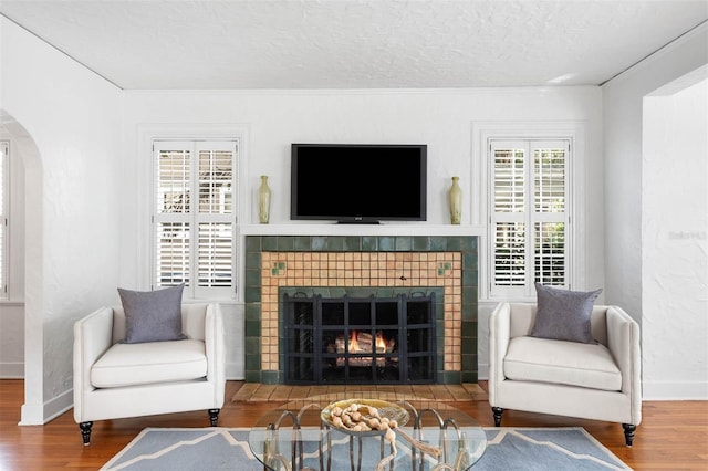 living room with wood-type flooring, a textured ceiling, and a tiled fireplace