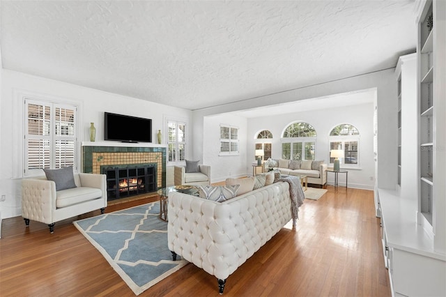 living room featuring a tiled fireplace, a wealth of natural light, wood-type flooring, and a textured ceiling