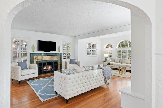 living room with a tile fireplace, a textured ceiling, hardwood / wood-style flooring, and plenty of natural light