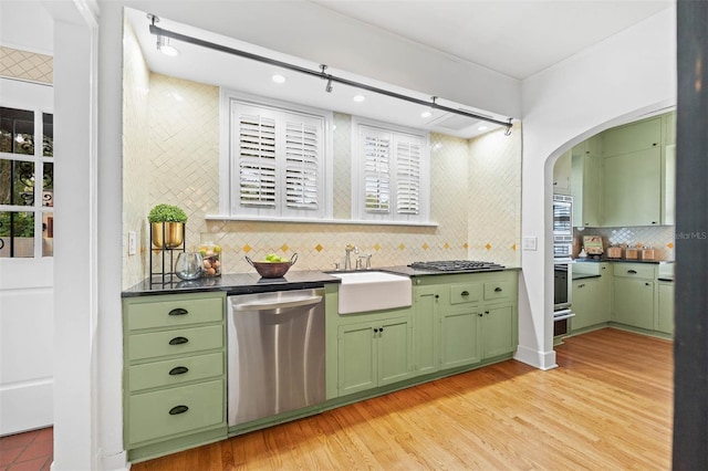 bar with stainless steel dishwasher, decorative backsplash, green cabinets, and light hardwood / wood-style flooring