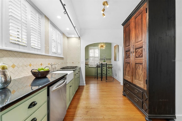 kitchen with sink, rail lighting, light hardwood / wood-style flooring, stainless steel dishwasher, and decorative backsplash