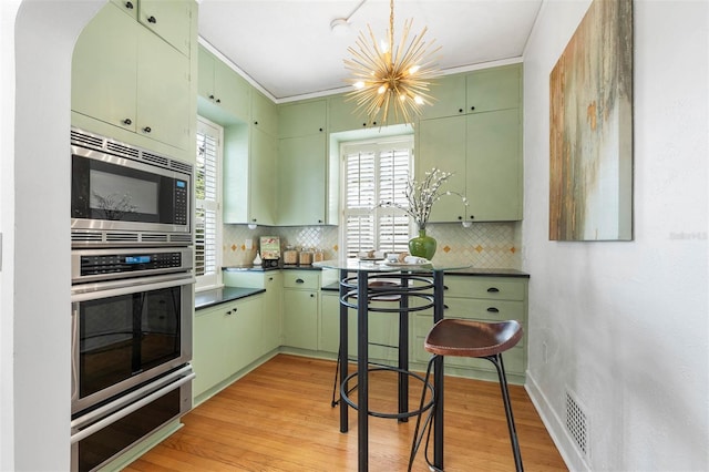 kitchen featuring an inviting chandelier, green cabinets, light hardwood / wood-style flooring, decorative backsplash, and appliances with stainless steel finishes