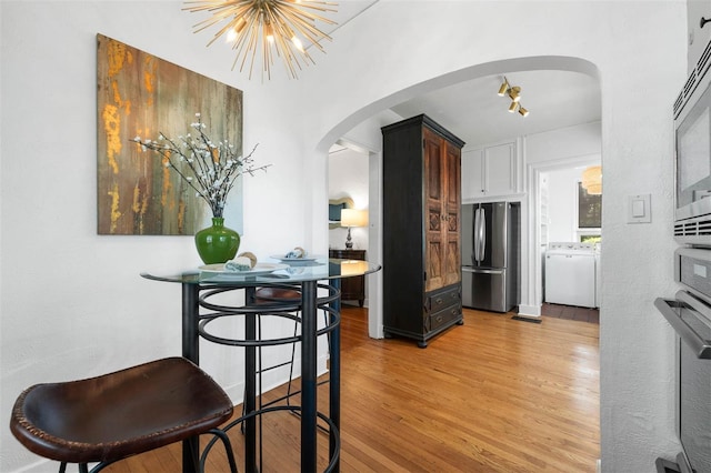 kitchen featuring dark brown cabinetry, stainless steel appliances, a chandelier, light hardwood / wood-style floors, and washer / dryer