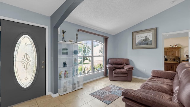 foyer entrance with vaulted ceiling, a textured ceiling, and light tile patterned flooring