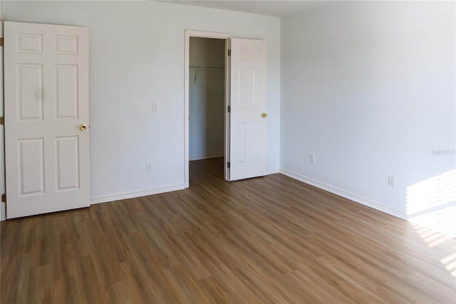 unfurnished bedroom with a walk in closet, a closet, and dark wood-type flooring