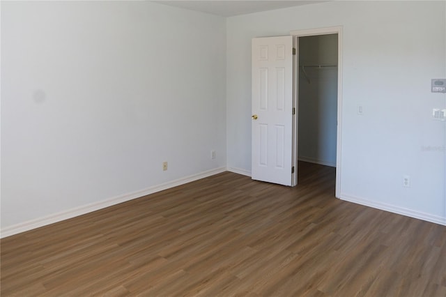 unfurnished bedroom with a spacious closet, a closet, and dark wood-type flooring