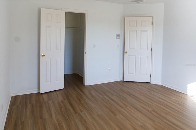 unfurnished bedroom featuring a spacious closet, dark wood-type flooring, and a closet