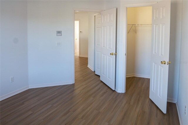 unfurnished bedroom with a spacious closet, a closet, and dark wood-type flooring