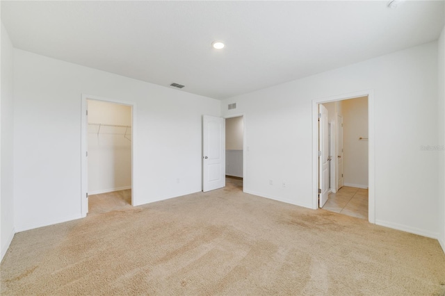 unfurnished bedroom with light carpet, ensuite bath, a closet, and a walk in closet