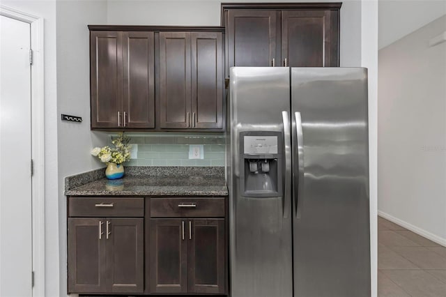 kitchen featuring backsplash, dark stone counters, dark brown cabinets, light tile patterned flooring, and stainless steel fridge with ice dispenser