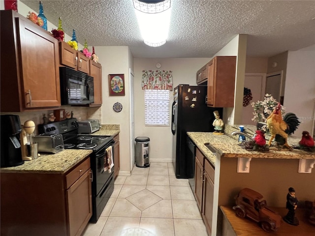 kitchen with light tile patterned floors, brown cabinetry, a textured ceiling, black appliances, and a sink