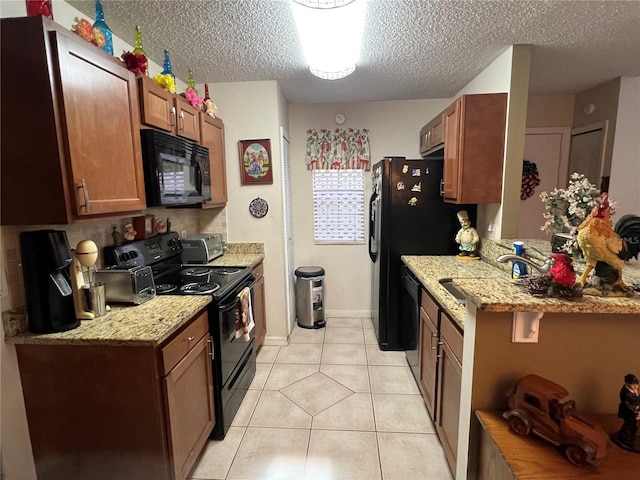 kitchen with light tile patterned floors, a sink, a textured ceiling, brown cabinets, and black appliances