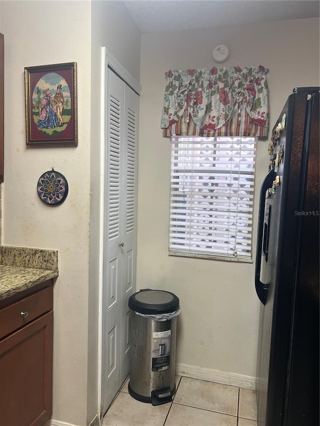 kitchen with light tile patterned flooring, stone countertops, and black fridge