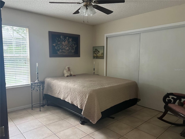 bedroom with a closet, a ceiling fan, light tile patterned floors, and a textured ceiling