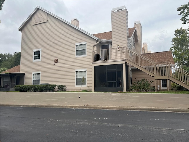 back of house featuring stairway, a sunroom, a balcony, and a chimney