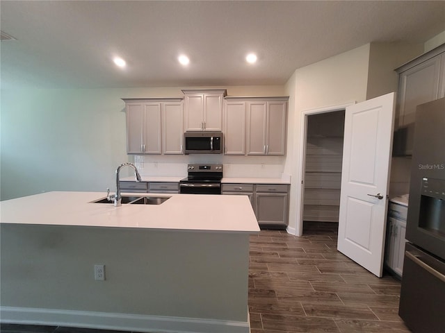 kitchen with a kitchen island with sink, appliances with stainless steel finishes, sink, and gray cabinetry