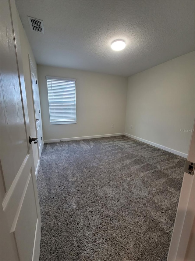 spare room with dark colored carpet and a textured ceiling