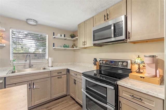 kitchen featuring light wood-type flooring, a textured ceiling, appliances with stainless steel finishes, and sink