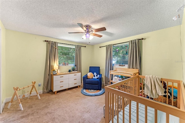 carpeted bedroom featuring a textured ceiling, a crib, and ceiling fan