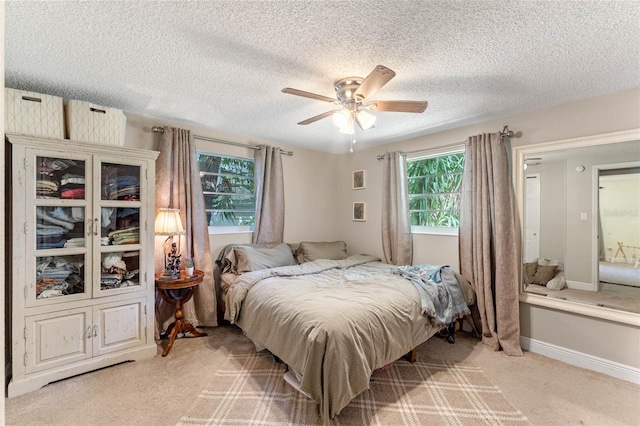 bedroom with ceiling fan, light colored carpet, and a textured ceiling