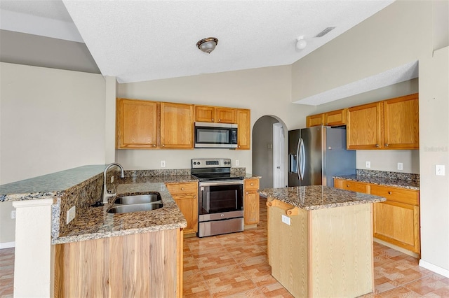 kitchen featuring sink, kitchen peninsula, appliances with stainless steel finishes, a center island, and vaulted ceiling