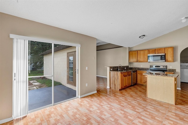 kitchen featuring dark stone countertops, vaulted ceiling, stainless steel appliances, a textured ceiling, and sink