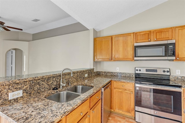 kitchen with ceiling fan, sink, stone counters, appliances with stainless steel finishes, and vaulted ceiling