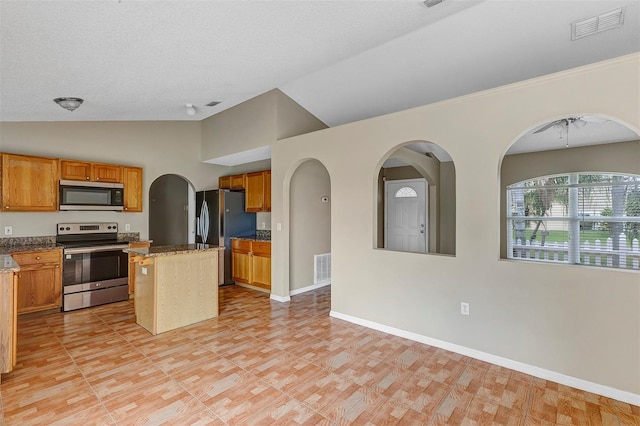 kitchen with lofted ceiling, a kitchen bar, stone counters, a kitchen island, and stainless steel appliances