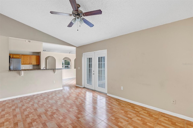 unfurnished living room with ceiling fan, light hardwood / wood-style floors, french doors, a textured ceiling, and vaulted ceiling