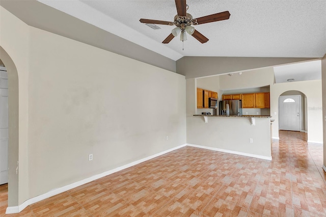 unfurnished living room with ceiling fan, a textured ceiling, light hardwood / wood-style floors, and vaulted ceiling