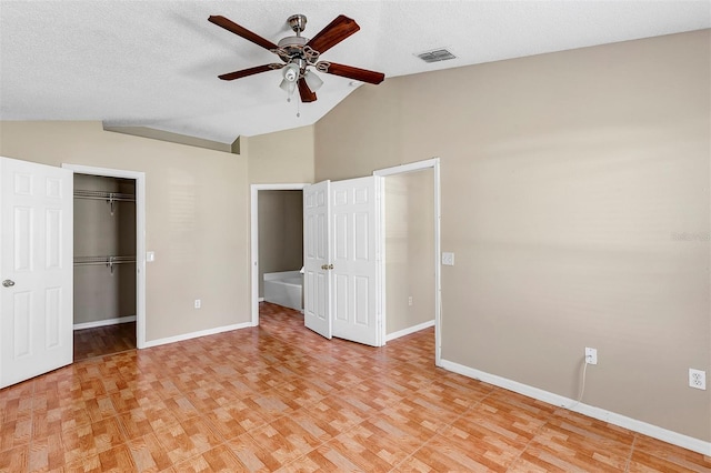 unfurnished bedroom with vaulted ceiling, a spacious closet, connected bathroom, a textured ceiling, and ceiling fan