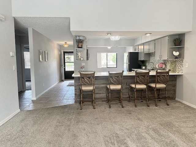 kitchen featuring a kitchen breakfast bar, carpet flooring, decorative backsplash, kitchen peninsula, and stainless steel refrigerator