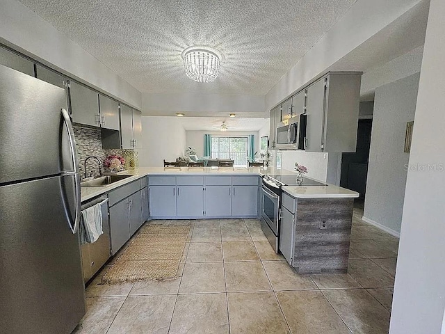 kitchen with sink, a textured ceiling, appliances with stainless steel finishes, tasteful backsplash, and kitchen peninsula