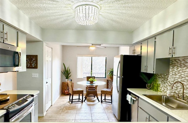 kitchen featuring tasteful backsplash, ceiling fan with notable chandelier, stainless steel appliances, sink, and light tile patterned floors