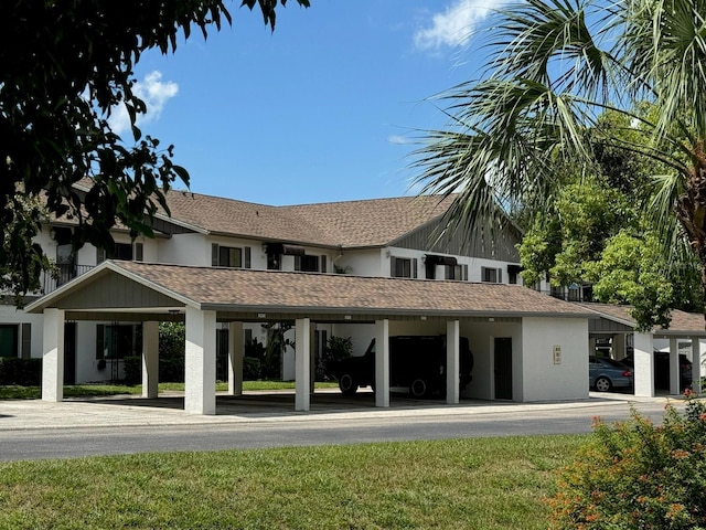 back of house with covered parking, roof with shingles, and stucco siding