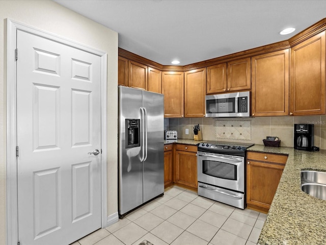 kitchen featuring light stone counters, brown cabinets, decorative backsplash, and stainless steel appliances