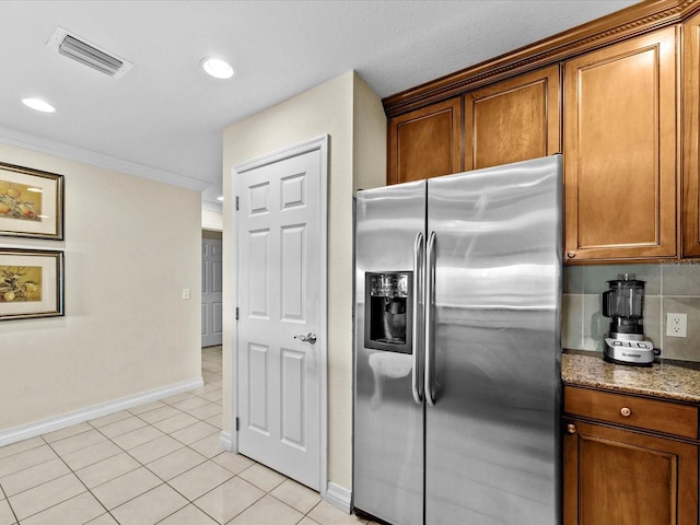 kitchen featuring tasteful backsplash, light tile patterned floors, dark stone counters, ornamental molding, and stainless steel fridge with ice dispenser