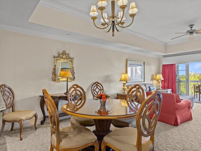 carpeted dining space featuring ceiling fan with notable chandelier, a tray ceiling, and crown molding