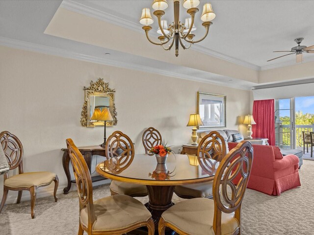 carpeted dining room featuring ceiling fan with notable chandelier, ornamental molding, and a raised ceiling