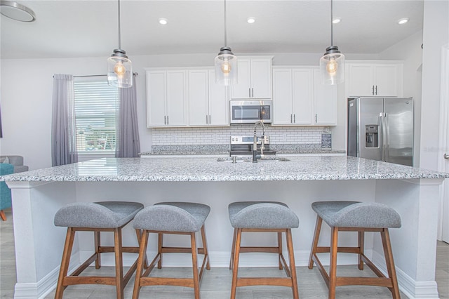 kitchen with appliances with stainless steel finishes, hanging light fixtures, white cabinets, light stone countertops, and a spacious island