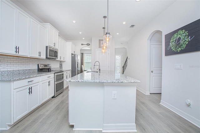 kitchen with hanging light fixtures, light hardwood / wood-style floors, white cabinetry, stainless steel appliances, and a kitchen island with sink