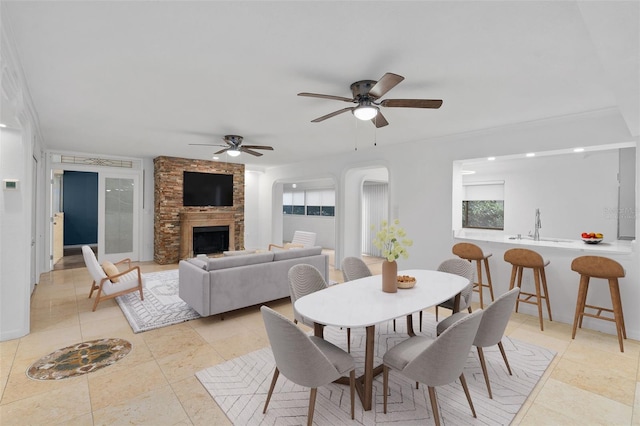 tiled dining space featuring a fireplace, sink, and ceiling fan