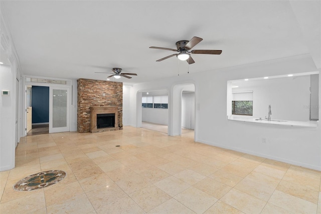 unfurnished living room featuring crown molding, a stone fireplace, and ceiling fan